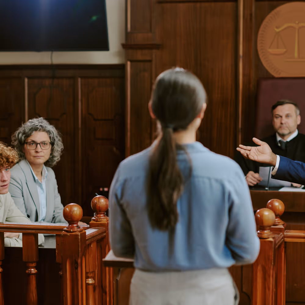 Woman facing judge and jury in courtroom during legal proceeding.