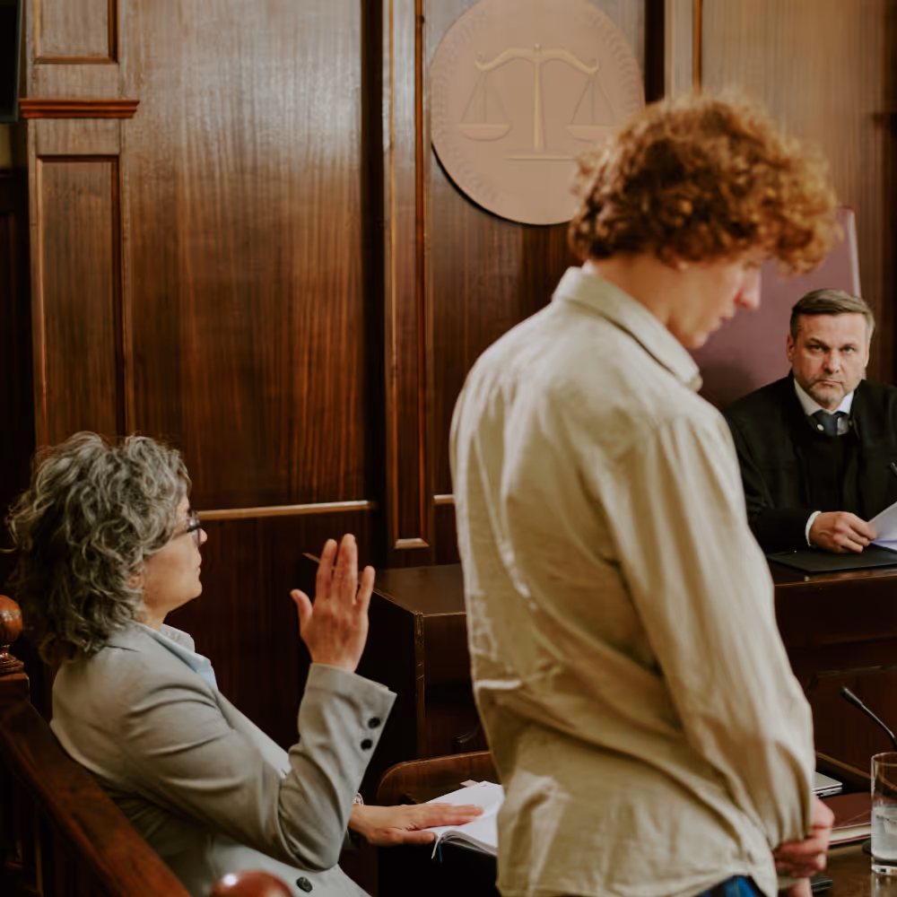 Lawyer raising hand in court while a young man stands before a judge holding papers.